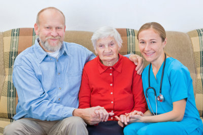 a chaplain, an elderly woman, and a nurse sitting on the sofa together and smiling